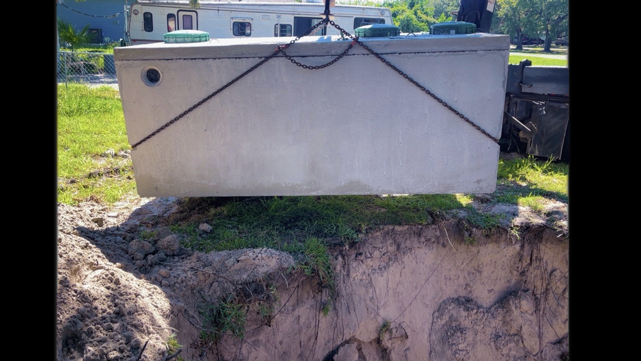Concrete septic tank suspended on chains above an open excavation